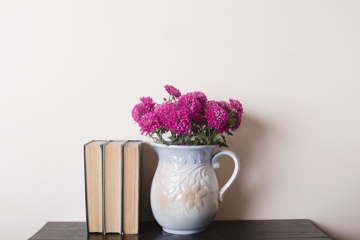 Pink chrysanthemum in a clay rarity vase and books on a wooden table, light background. Copyspace.